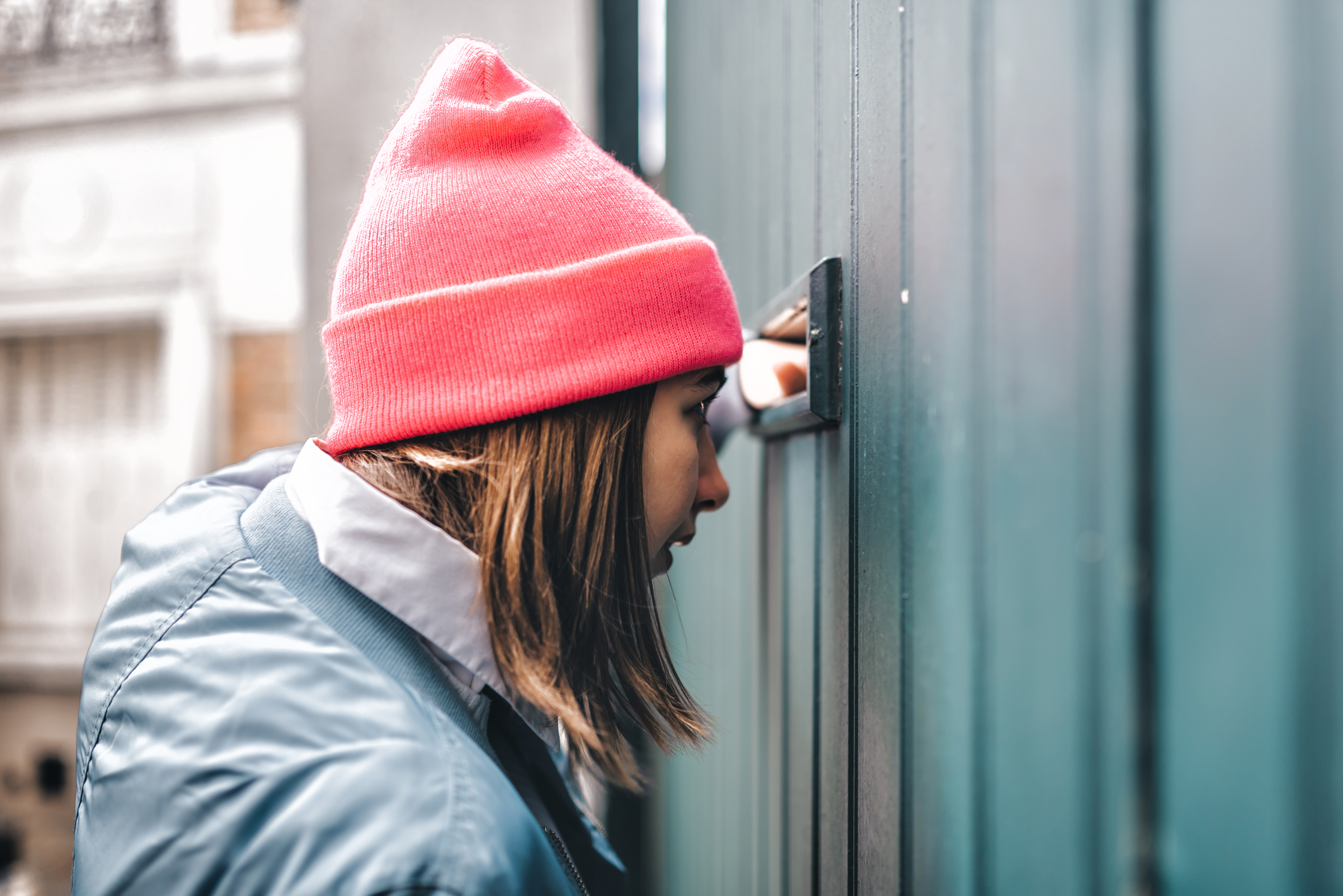 Junge Frau mit Mütze schaut durch einen Spalt in der Wand