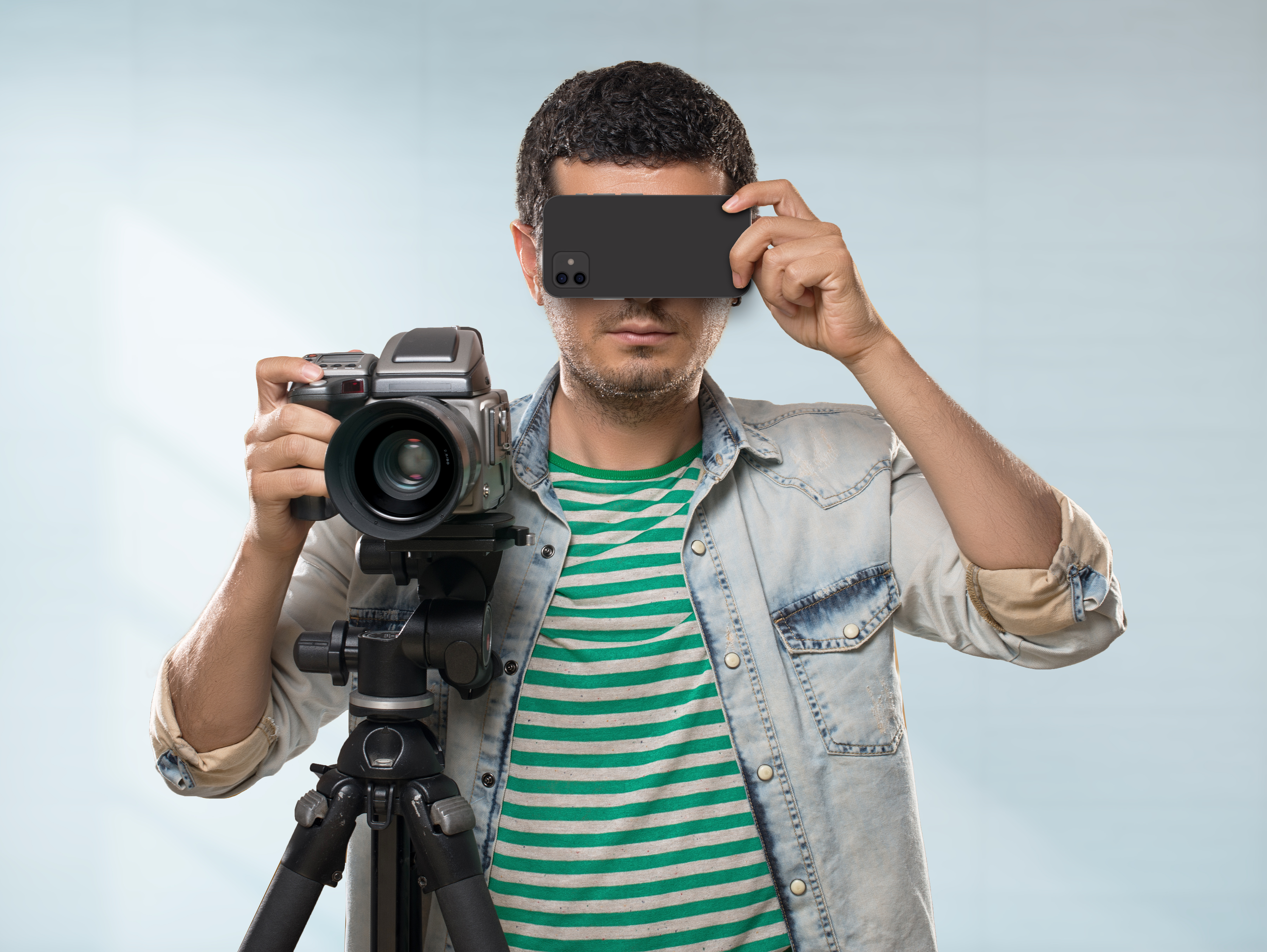 Fotograf hält Smartphone vor seinen Augen und mit der anderen Hand eine Kamera auf dem Stativ