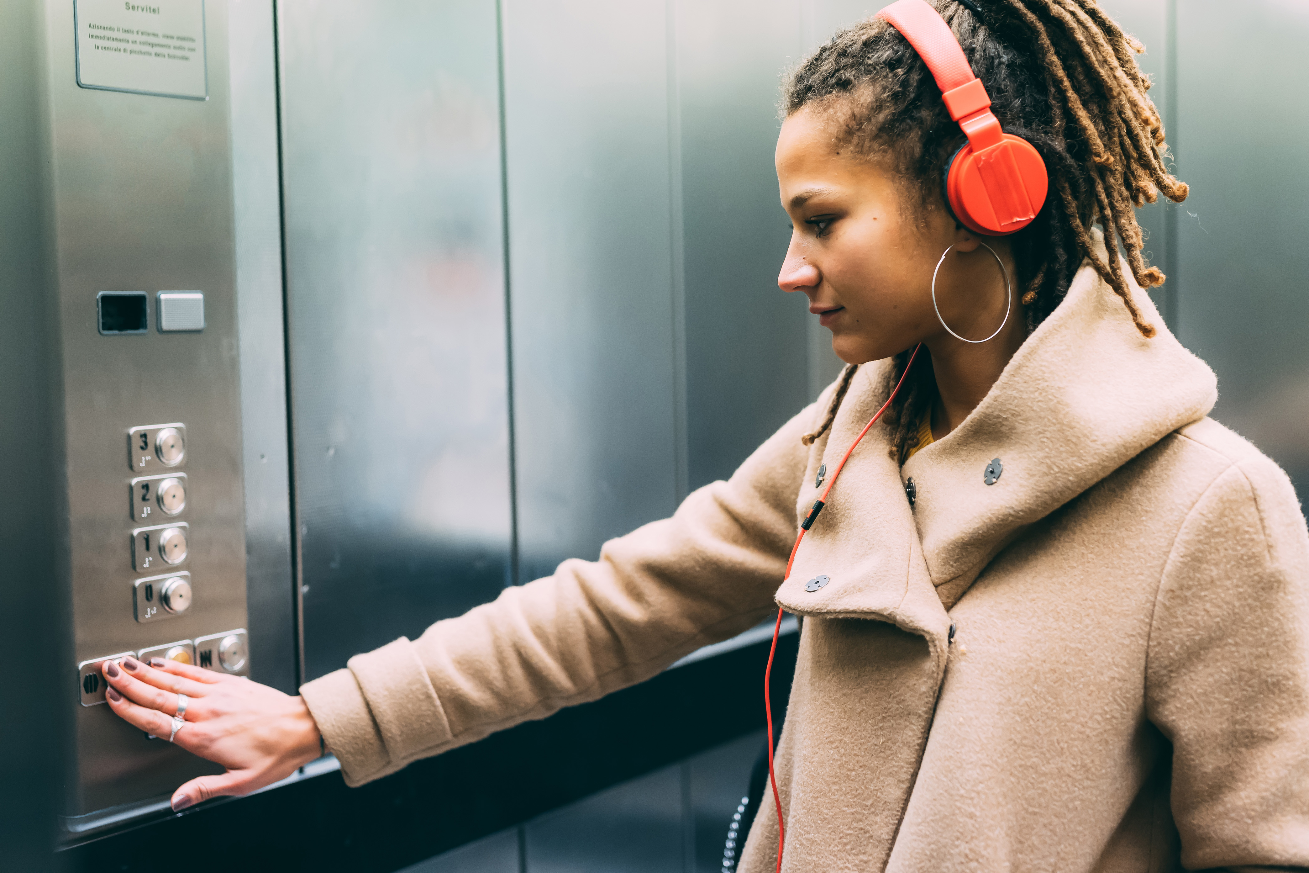 Junge Frau mit roten Kopfhörern drückt eine Taste im Lift.