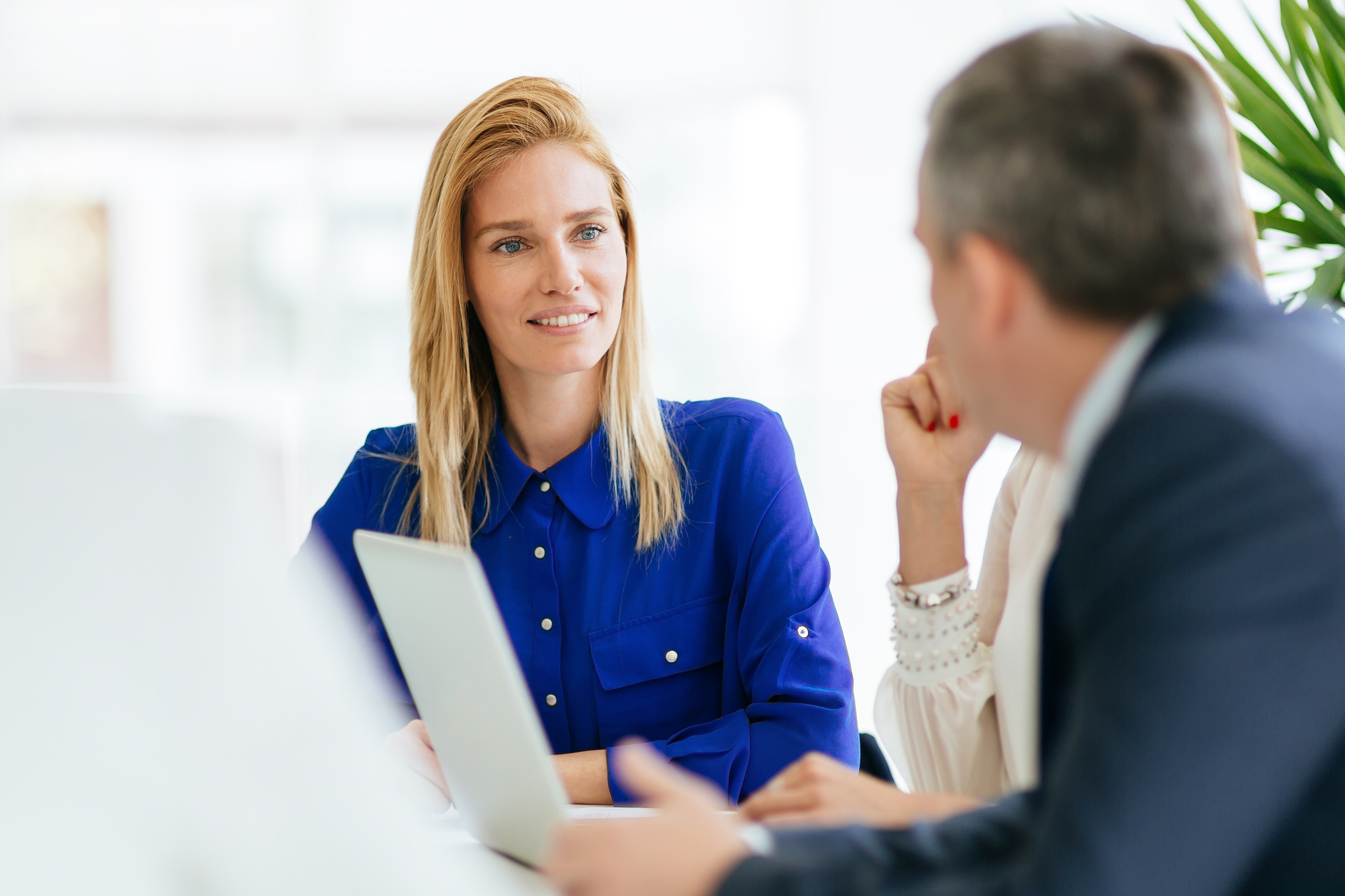 Jüngere blonde Frau in Verhandlung mit einer anderen Dame und einem Herrn in blauer Kleidung.